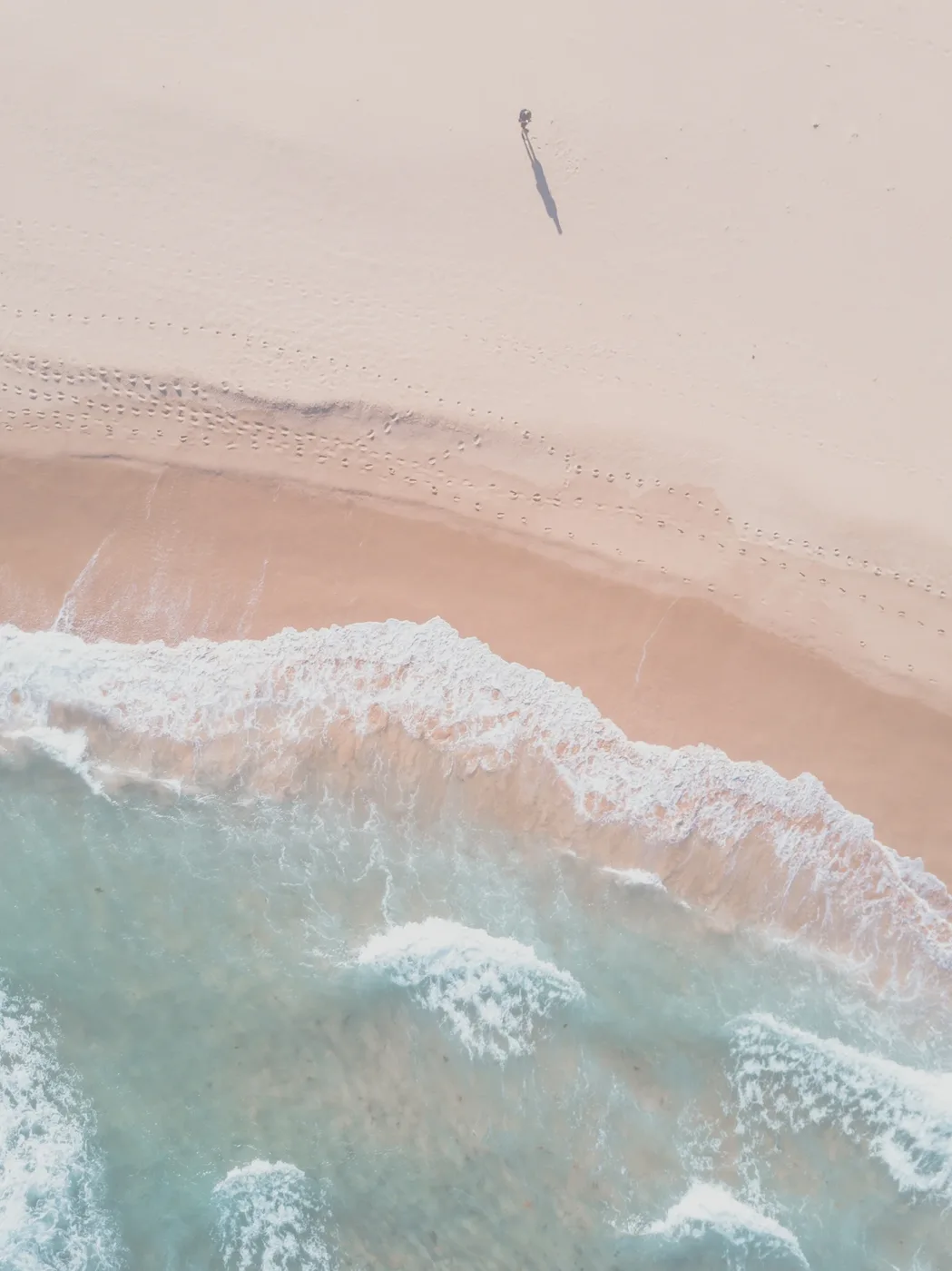 Plage vue du ciel aux tons pastel, vaguelettes et sable rosé — respiration et calme collectif, sophrologie en entreprise