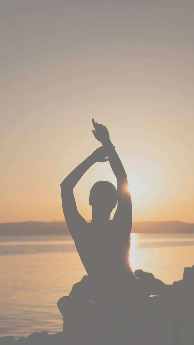 Silhouette d'une femme s'étirant face à la mer au coucher du soleil — lâcher-prise et sérénité, sophrologie en visio avec Clara Dudoit
